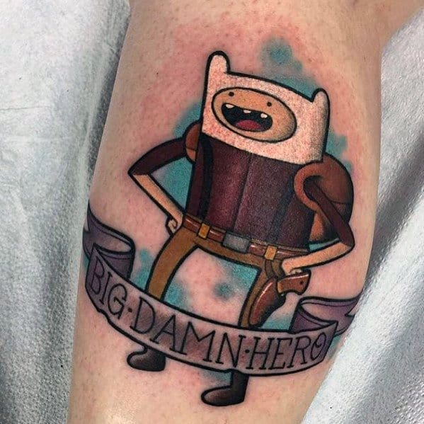 Adventure Time tattoo of Finn dressed as a cowboy with a banner reading "BIG DAMN HERO," inked on the upper leg.