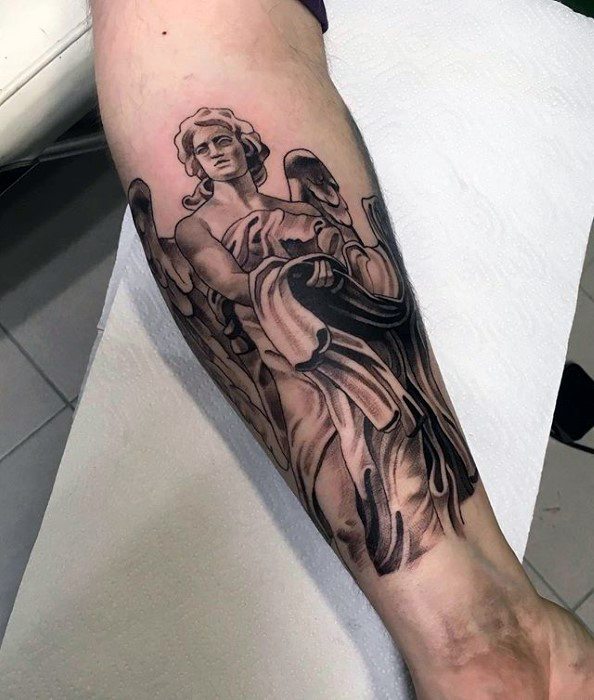 A black and grey tattoo on the lower leg featuring an angel with large wings, depicted in a dynamic pose with flowing robes and detailed shading.