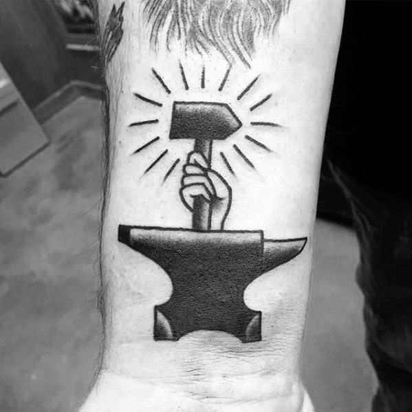 Bold black anvil tattoo with a hand rising from it holding a hammer, surrounded by radiant lines for a powerful and symbolic design.