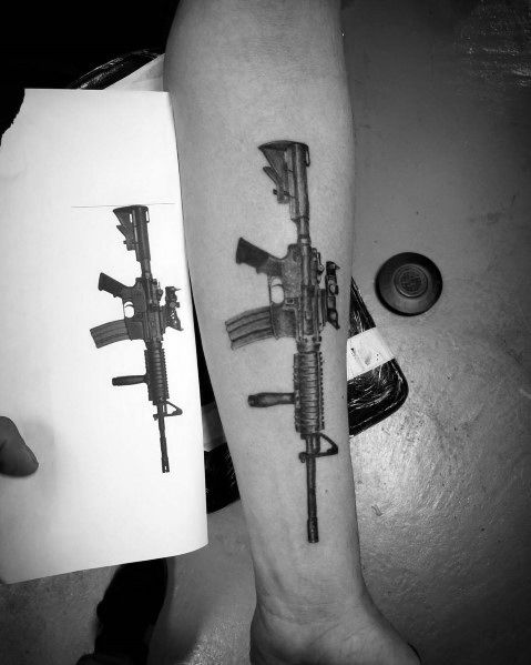Black and grey AR-15 tattoo on the forearm, showcasing a highly detailed design with a tactical grip, scope, and magazine for a realistic look.