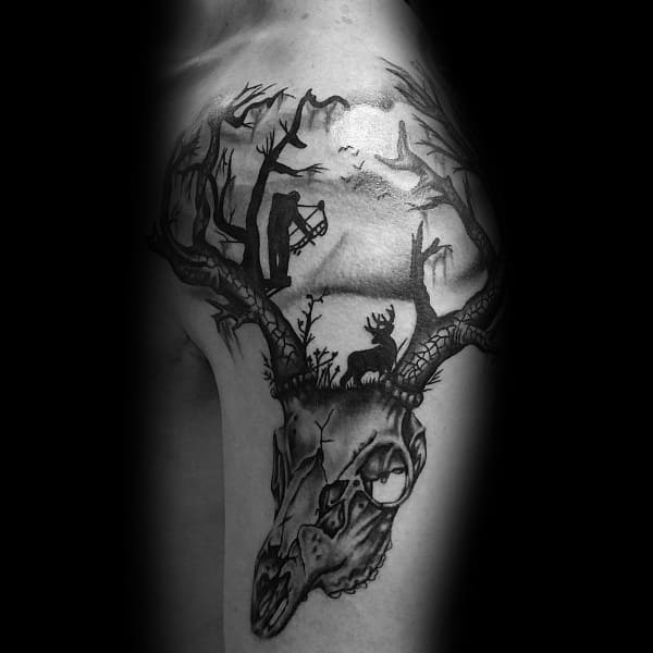 Black and grey upper arm tattoo of a deer skull with antlers forming a forest scene, featuring a bowhunter and a deer under a full moon.