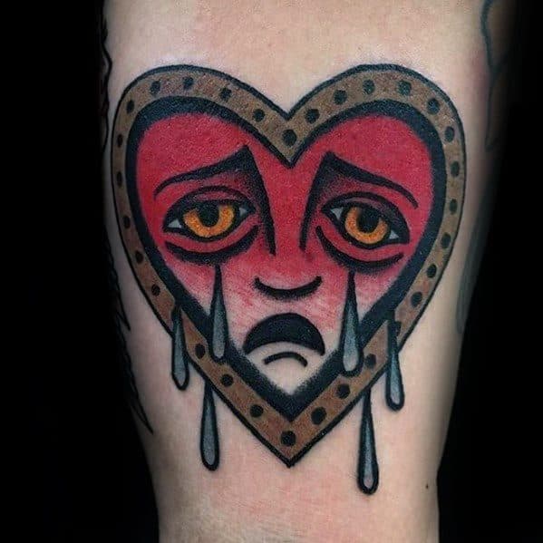 Tattoo of a heart-shaped face with sad eyes and tears, surrounded by a dotted outline
