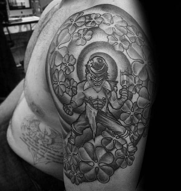 Black and grey tattoo of a menacing leprechaun with a knife, surrounded by swirling shamrocks and a glowing halo-like backdrop.