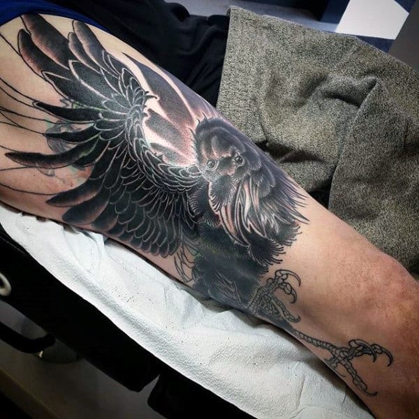 Arm tattoo featuring a detailed, black-feathered raven with wings spread and sharp talons