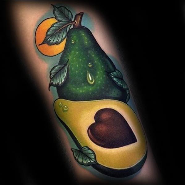 Bold and vibrant avocado tattoo with a heart-shaped pit, paired with a whole avocado and leafy details, under a glowing sun.