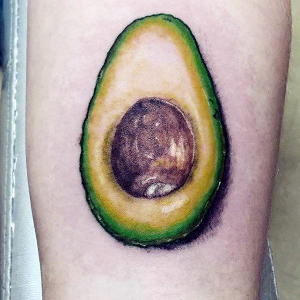 Realistic avocado tattoo with detailed shading and texture, highlighting the creamy flesh and rich brown seed on a soft-toned background.