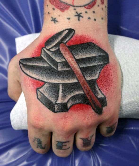 Traditional anvil tattoo on the hand with a hammer resting on top, bold black shading, and vibrant red background for a striking contrast.
