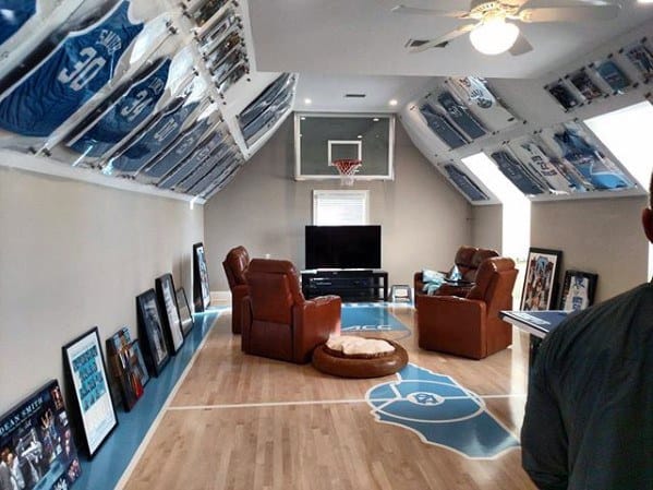 Room with sports jerseys on the walls, basketball hoop, leather chairs, and a TV; basketball court floor design