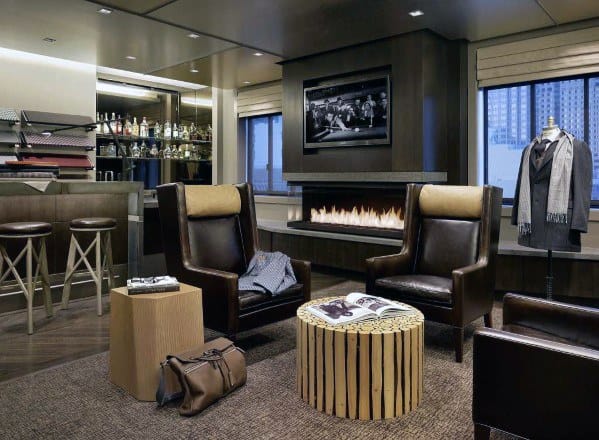 Stylish lounge with leather chairs, bar, fireplace, and city view through windows; cozy and modern ambiance