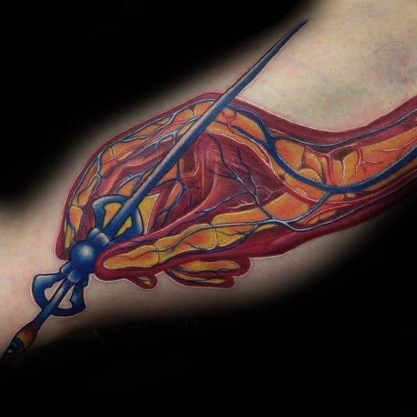 Anatomical-style Tool-inspired tattoo on the arm showing exposed muscles, veins, and a blue spear piercing through the design.