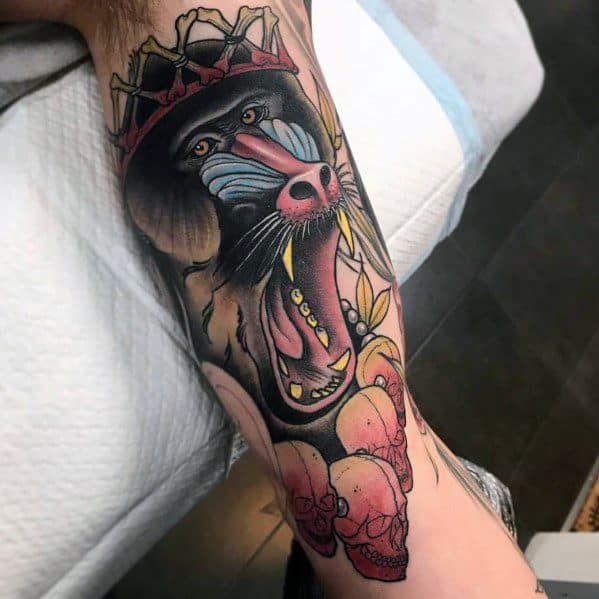 Neo-traditional baboon tattoo with bold colors, fierce expression, and a crown of thorns, featuring skulls and intricate shading for a striking design.