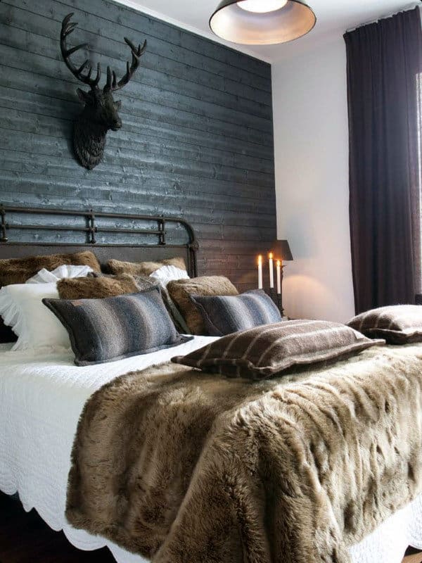 Cozy bedroom with fur bedding, pillows, dark wood panel wall, and deer head decor
