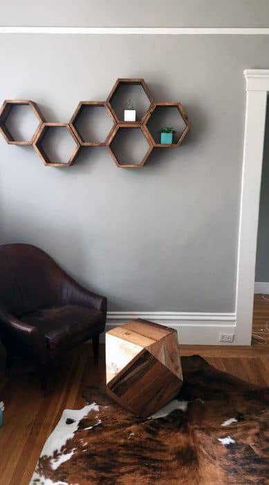 Hexagon wooden shelf with minimalist decor on a gray wall above a leather chair and cowhide rug.