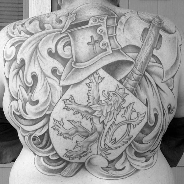 Full back tattoo in black and grey featuring a knight’s helmet, axe, and a detailed shield with a roaring lion and ornamental flourishes.