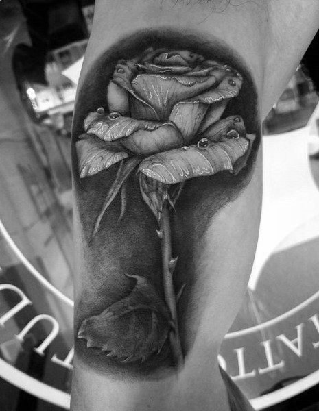 Black and gray tattoo of a rose with detailed shading, water droplets on petals, and a gracefully curved stem