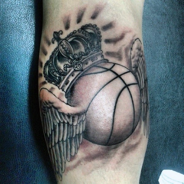Tattoo of a crowned basketball with angel wings on the inner side of the leg
