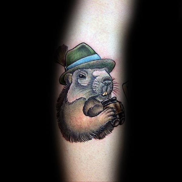 Whimsical tattoo of a groundhog wearing a green hat and holding binoculars, blending adventure and charm in a playful design.