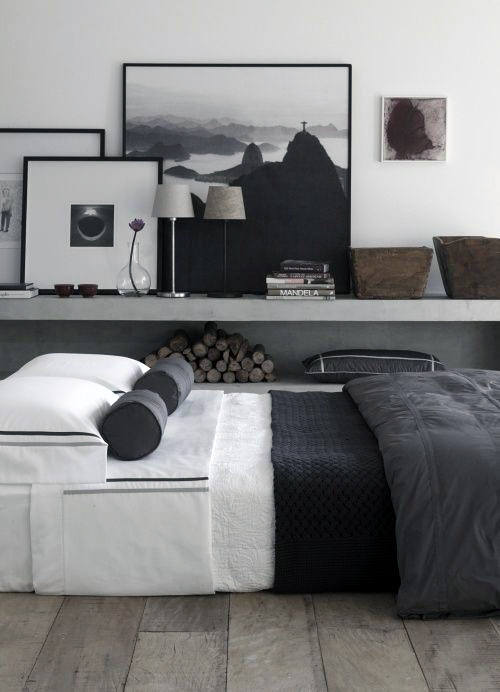 Minimalist bedroom with black and white decor, framed art, and stacked firewood.