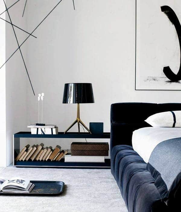 Modern bedroom with a black lamp, books, and art on a minimalist bedside table