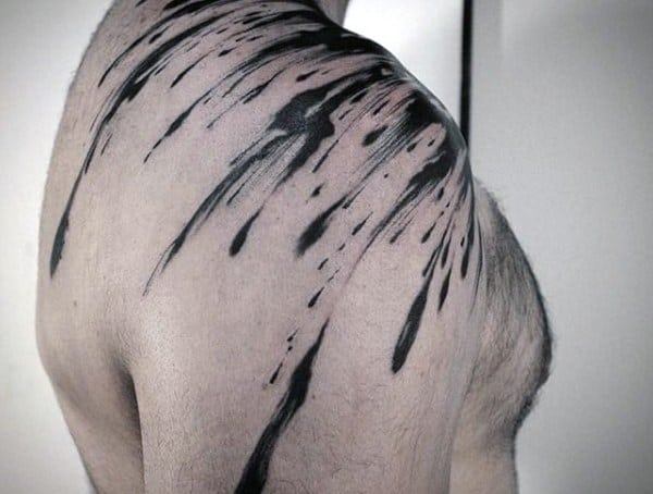 Shoulder tattoo for men featuring bold black ink splatter streaks flowing from the shoulder to the upper arm and back.