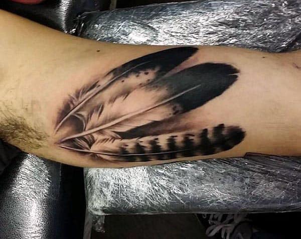 Black and grey realistic feather tattoo on the inner bicep, featuring intricate shading and fine details for a soft, natural look