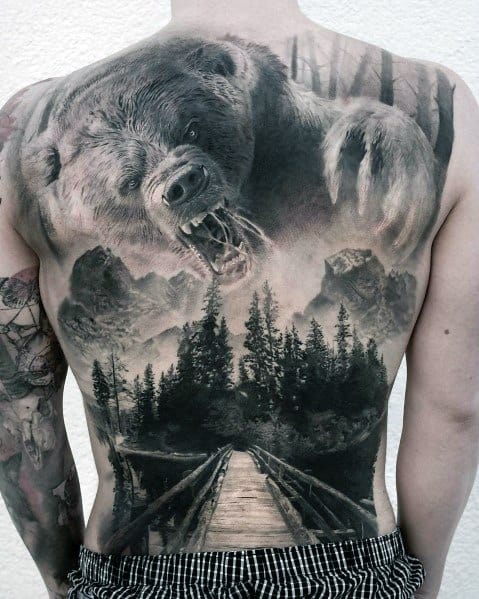 Realistic full-back tattoo featuring a roaring bear emerging from a misty forest, with a detailed wooden bridge leading into the wilderness.