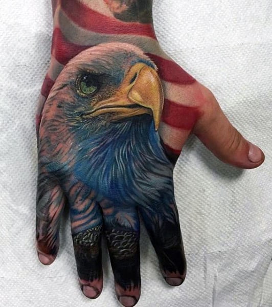 Detailed tattoo of a bald eagle on a hand, with an American flag in the background