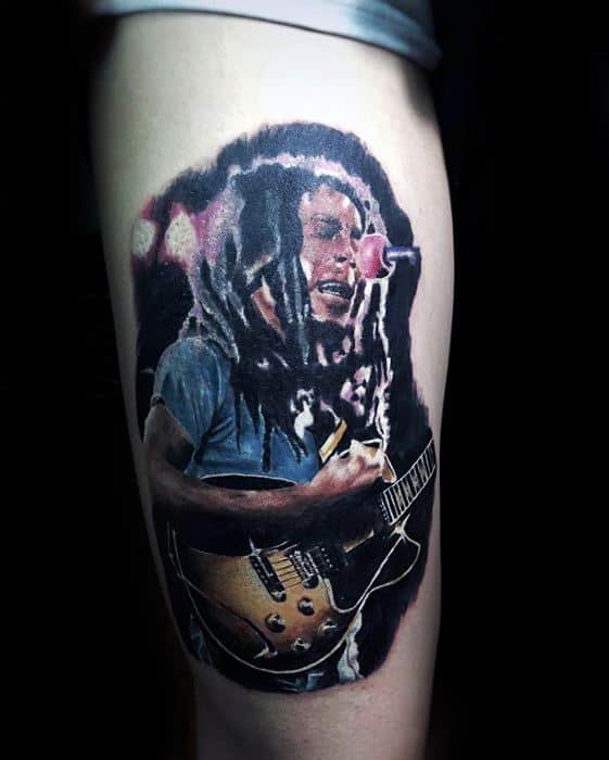 Vibrant thigh tattoo of Bob Marley performing with a guitar, featuring colorful lighting effects and dynamic stage energy in a realistic style.