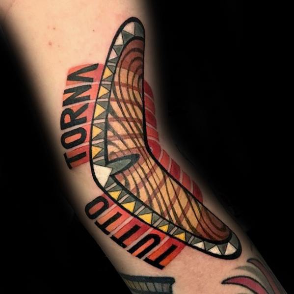 Bold boomerang tattoo with tribal-style lines and patterns, surrounded by the words TUTTO TORNA in block red and black letters.