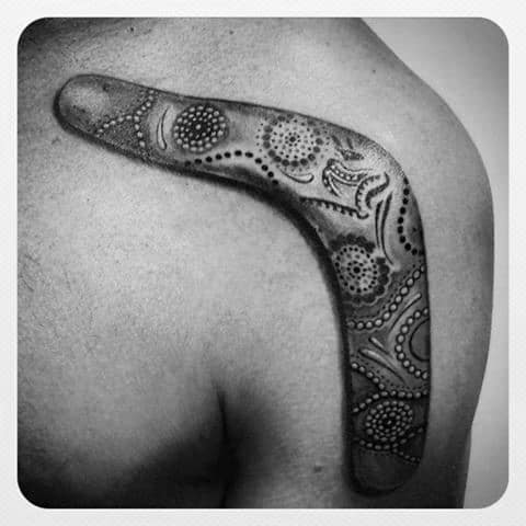 Large boomerang tattoo on the shoulder featuring intricate dotwork and Aboriginal-inspired patterns in black and grey ink.