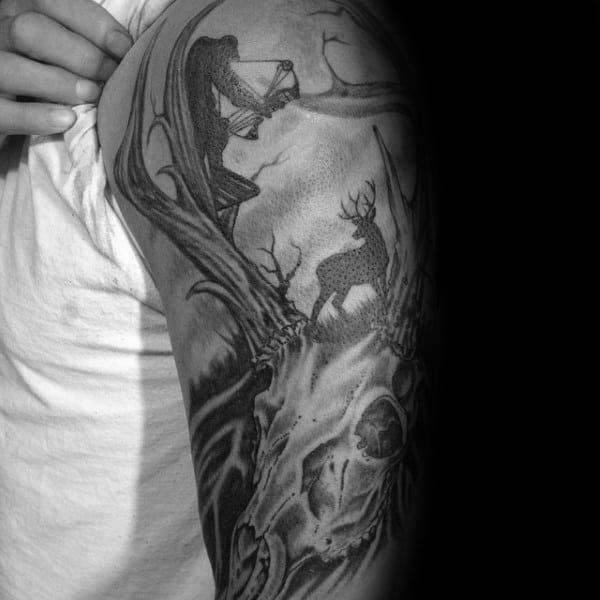 Black and grey shoulder tattoo of a detailed deer skull with antlers transforming into a forest scene, featuring a bowhunter aiming at a buck.