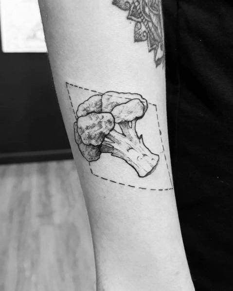 Minimalist black ink broccoli tattoo on the forearm, featuring fine linework and a dashed geometric frame for a modern and artistic look.