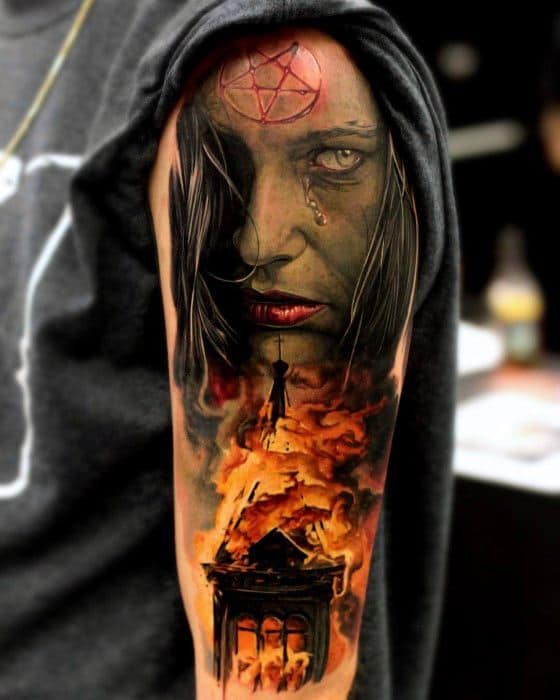 Realistic burning church tattoo with vivid flames below a haunting woman’s face. A pentagram on her forehead and teardrops enhance the eerie vibe.