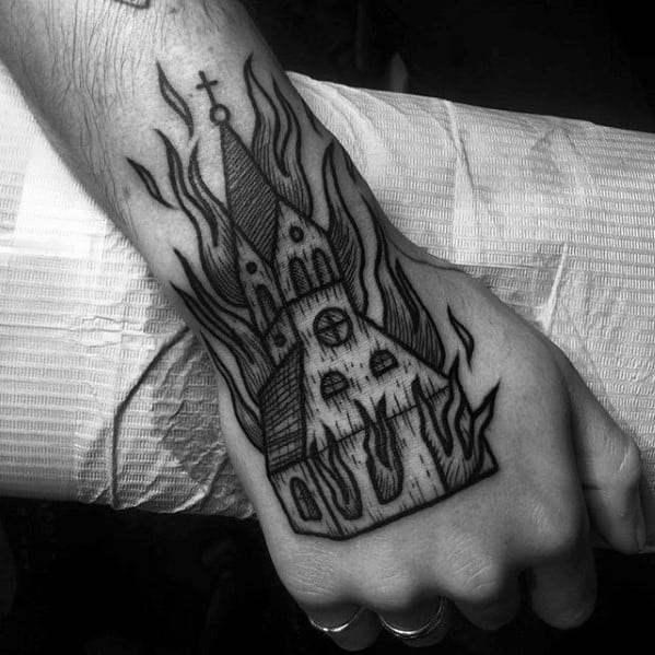 Black linework tattoo of a burning church placed on the hand. Sharp flames and gothic architecture create a bold and intense visual effect.
