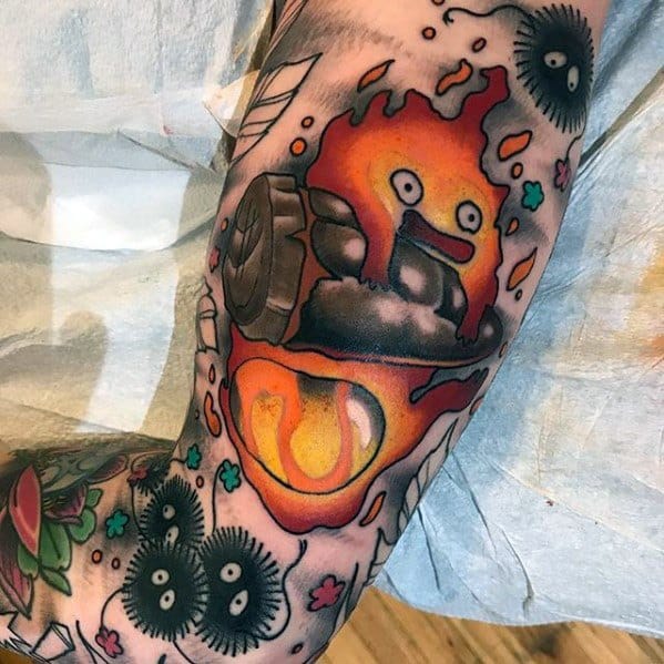 Vibrant sleeve tattoo of Calcifer holding a log, surrounded by Soot Sprites, falling leaves, and colorful flame details.