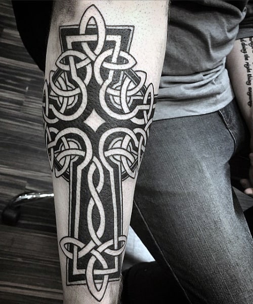 Forearm tattoo of an intricate Celtic cross with knotwork design