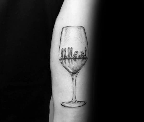 Black and grey tattoo of a champagne glass filled with a city skyline, blending urban architecture with a fine dotwork shading style.