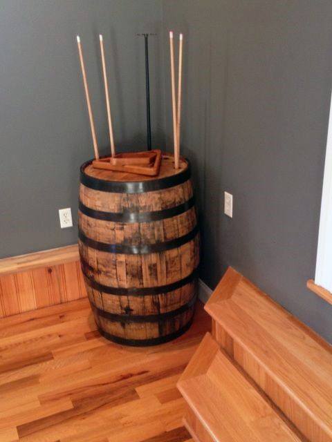 Wooden barrel with pool cues in a corner, next to wooden stairs and grey walls