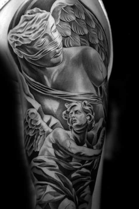 A black and grey tattoo on the upper arm depicting an angel holding another figure, with flowing robes and a sculpted blindfolded figure.