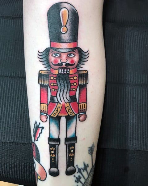 Traditional Christmas tattoo of a classic nutcracker soldier in a red and gold uniform, featuring bold lines and festive details for a vintage holiday look.