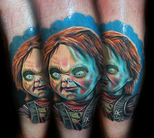 Realistic Chucky tattoo with eerie green and blue lighting, featuring his sinister grin, intense eyes, and detailed horror-inspired shading.