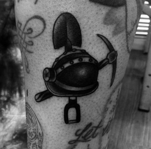 Black and grey tattoo of a miner's helmet with a shovel, pickaxe, and lantern arranged in a bold, compact design.