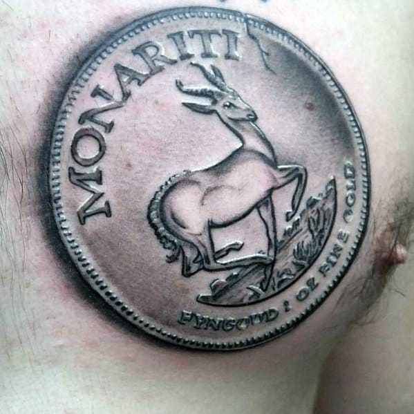 Realistic tattoo of a gold coin featuring a springbok and 'Monariti' text, placed on the chest with detailed shading for a 3D effect.
