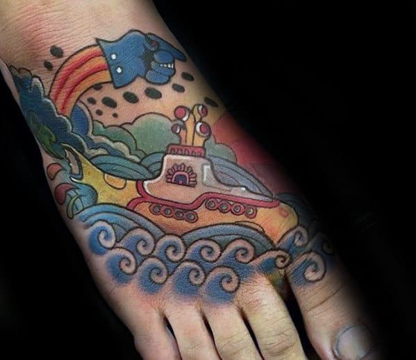 Vibrant foot tattoo of The Beatles' Yellow Submarine sailing on swirling waves, with colorful clouds, a rainbow, and the Blue Meanie above.