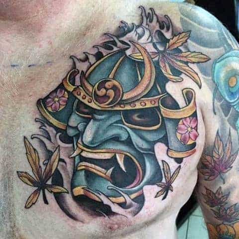 Vivid chest tattoo of a colorful samurai mask surrounded by delicate maple leaves, blending tradition with modern artistry