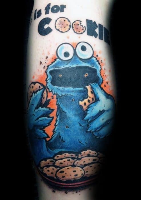 Colorful Cookie Monster tattoo with “C is for COOKIE” text, holding cookies with a full bowl below and vibrant orange accents.