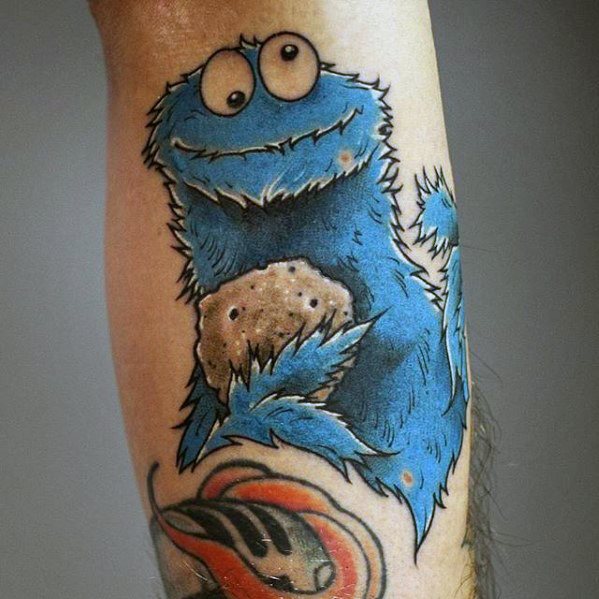 Cartoon-style Cookie Monster tattoo with a playful grin, holding a large cookie and outlined with bold black lines.