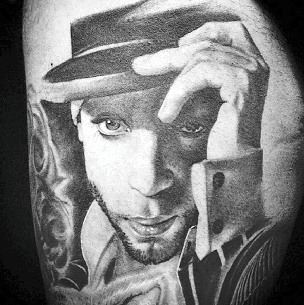 Tattoo of Prince in a hat with detailed shading on his face and a contemplative expression