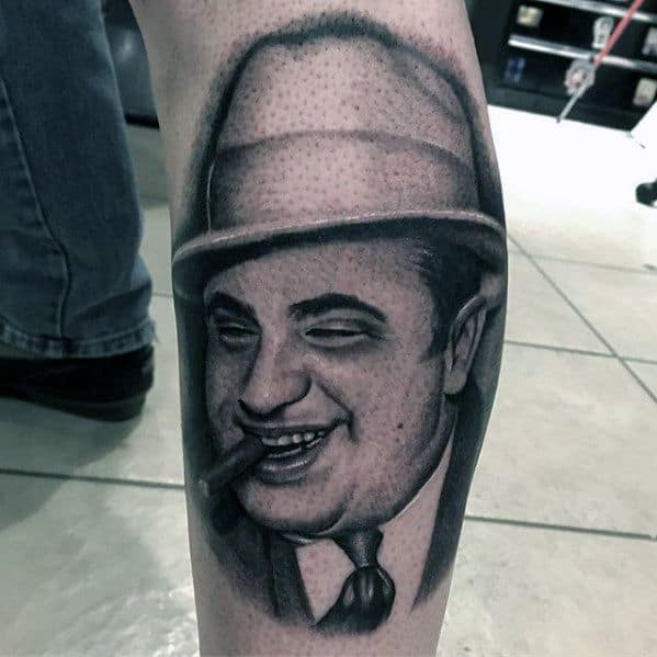 Al Capone tattoo featuring a detailed black-and-white portrait of the gangster smiling with a cigar, wearing his iconic fedora and suit.