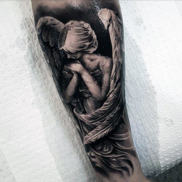 A black and grey tattoo on the forearm featuring an angel with large wings, holding a peaceful and contemplative pose, with detailed shading and soft textures.